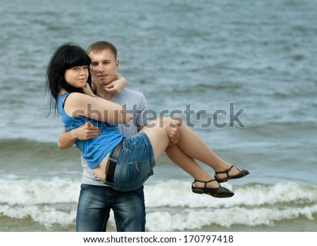 loving young couple is embracing at sea. Man is holding the woman on hands