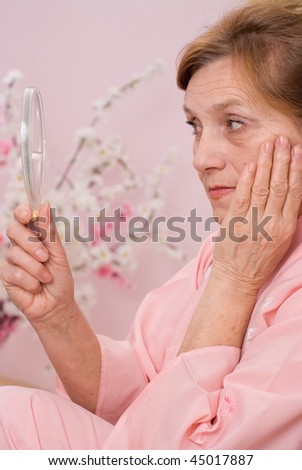 pretty  elderly woman sitting  and looks in the mirror