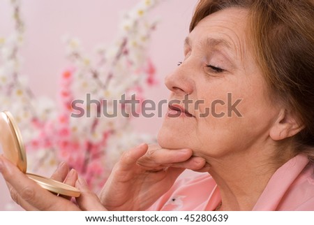 elderly woman examines her face in the mirror