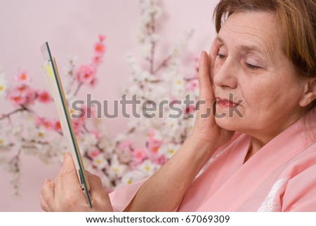elderly woman with a mirror on a pink background