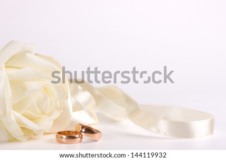 Bautiful pearly rose, wedding rings and ribbon over white
