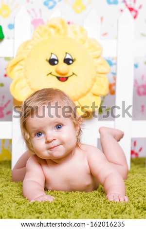 Cute little baby with big blue eyes  lies down on his stomach, smile and looks towards