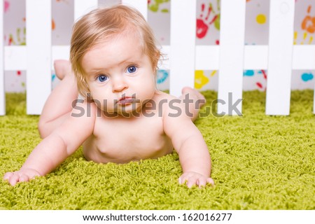 Pretty baby with big blue eyes  lies down on his stomach and looks into camera