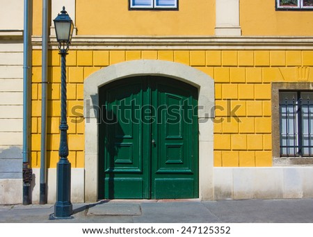 Fragment of european building with yellow wall, green door, windows and lantern.