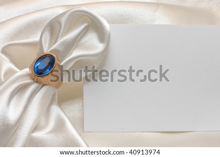 Golden napkin ring with sapphire, white satin napkin and card