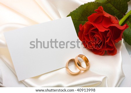 stock photo Two gold wedding rings red rose and card over white satin