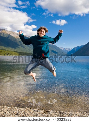 Young man jumps for joy out of a beautiful New Zealand lake, arms up.