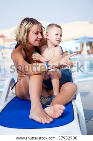 Young mum with the son sit on a chaise lounge, mum showing a finger aside