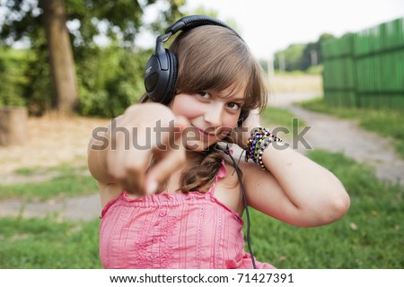 beautiful teenage girl in a pink dress with headphones to point the finger at the camera, focus on her face