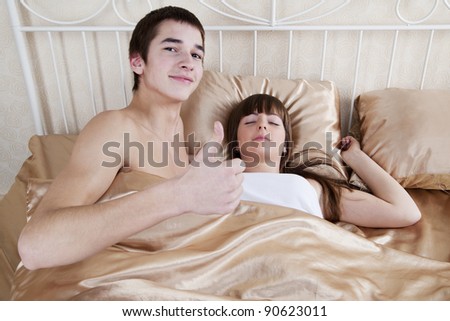 Couple in bedroom. A young man thumbs-up, a young woman sleeping
