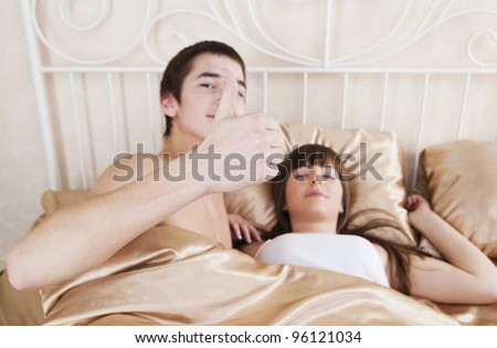Couple in bedroom. A young man shows thumbs-up, a young woman sleeping