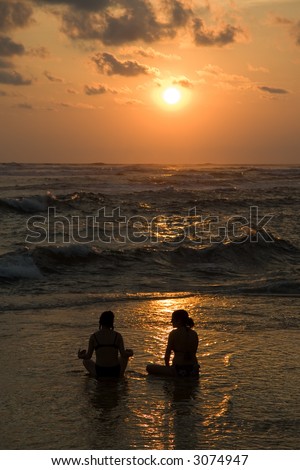Two woman in a Lotus position as the sun sets over the pacific