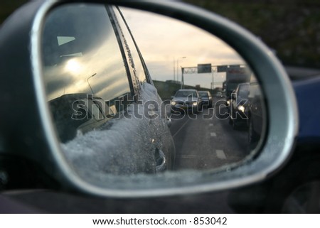 Car mirror in which you can see the snow on the car and other cars on the road.