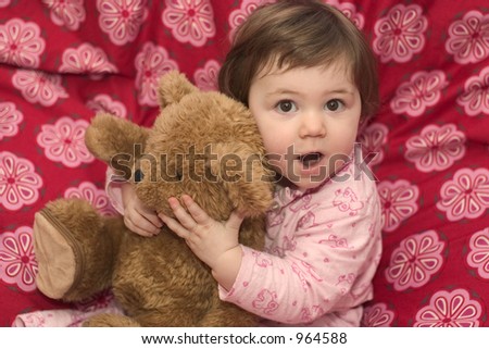 Little girl in Pyjamas on the bed, holding her teddybear, making faces