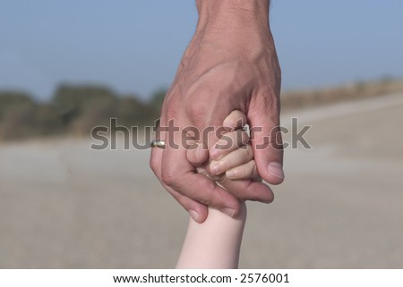 Child holding on to father\'s hand.