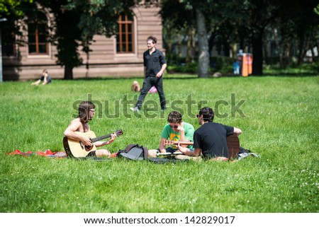 STUTTGART, GERMANY - June 15, 2013:  Students playing guitar and having fun in the park in front of the university on a bright summer day on June 15, 2013 in Stuttgart, Germany.