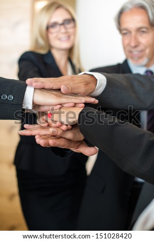Multiracial group of seven diverse businesspeople standing in a circle joining hands in a team with office scenario in the background. A businessman and a businesswoman is facing the camera smiling.