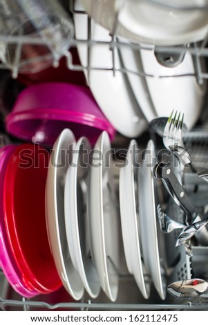 Dishwasher after cleaning process with plates, cups, glasses, cutlery and plastic boxes - shallow depth of field