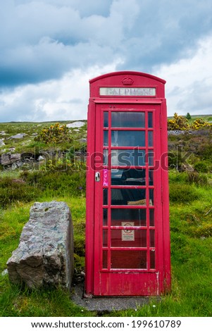 Old-fashioned traditional red telephone booth or public payphone standing next to an open deserted field in Scotland