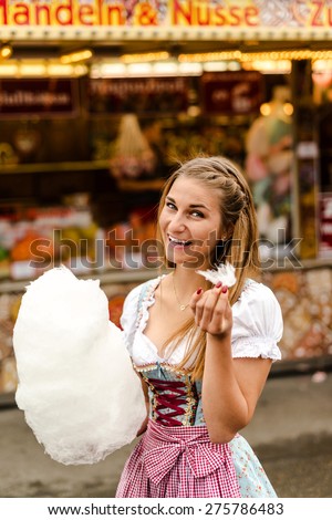 Beautiful woman wearing a traditional Dirndl dress with cotton candy floss at the Oktoberfest. The wording in the background says \