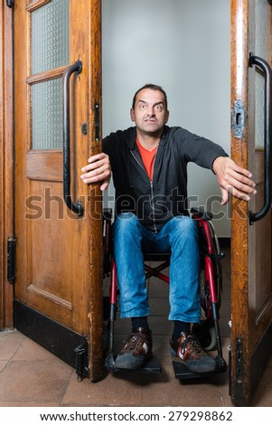A man in a wheelchair is stuck between swing doors, looking as if in panic and dismay