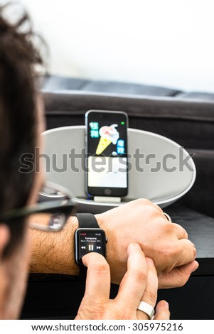 SCHARNHAUSEN, GERMANY - AUGUST 08, 2015: A man is controlling the playback of his Apple Music by using his Apple Watch to control his iPhone that is placed in a dock with loudspeakers in the