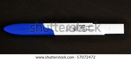 Positive Pregnancy Test on dark wooden table with ENGLISH text (pregnant, not pregnant)..