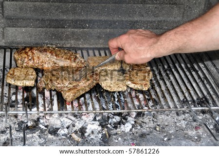 View into a stone BBQ with steaks and ribs above well burned coal - male hand is turning the steaks with a fork