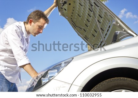 man repairing a broken car on a road