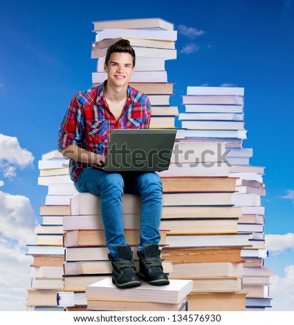 Young man sitting on a stack of books with a laptop,outdoors