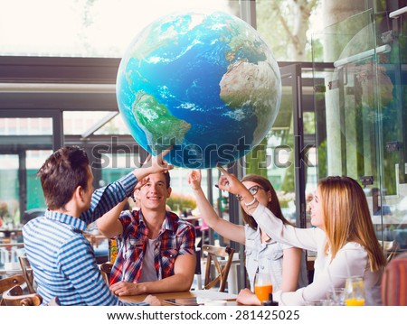 Group of young people pointing at planet Earth, sitting at the table. Elements of this image furnished by NASA