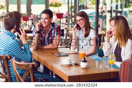 Group of young people sitting at a cafe, talking over mobile phones