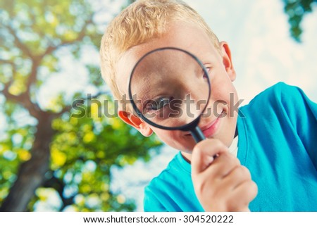 Cute boy in a park with a magnifying glass close up