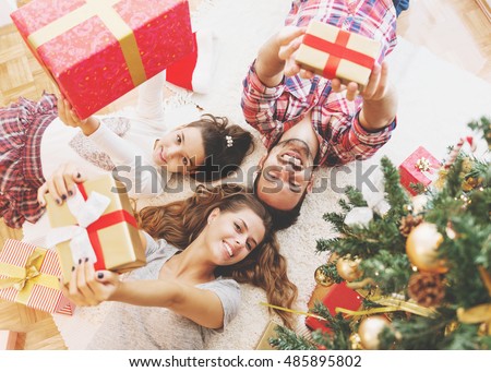 Family gather around a Christmas tree, holding presents