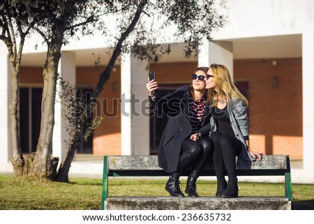 Two young university women taking selfie with mobile phone on the bench