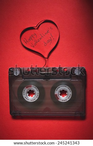 Retro audio cassette with magnetic tape in shape of heart on red background. Valentines day card