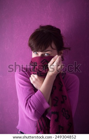 Beautiful young woman in pink sweater covers her face with the scarf on pink background.