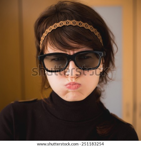 Hipster girl in glasses with puffed-out cheeks. Dissatisfied woman. Toned with color filter.