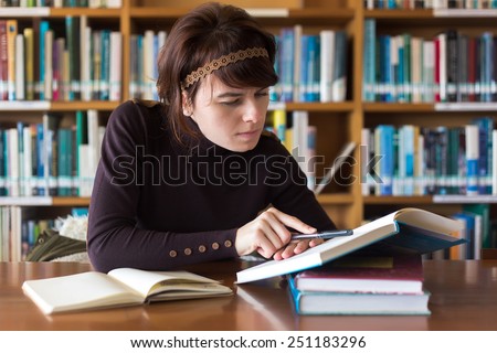 Beautiful student girl studying in college library. Looking for information in book. Selective focus on face.