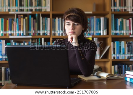 Student girl sitting with books and laptop computer in college library. Studying in university library. Selective focus on face.