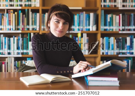Beautiful student girl studying in college library. Looking for information in book and smiling. Toned with filter. Selective focus on face.