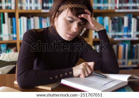 Student girl reading book in college library with perplexed face. Selective focus on face.