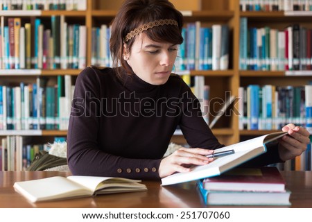 Beautiful student girl studying in college library. Looking for information in book. Selective focus on face.