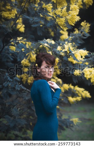 Beautiful young woman with yellow mimosa flowers. Art processing with color grading and shallow depth of field.