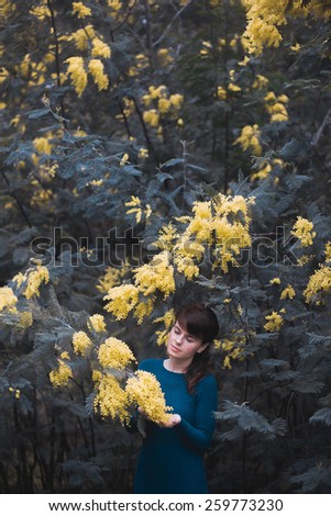 Beautiful young woman with yellow mimosa flowers. Art processing with color grading and shallow depth of field.