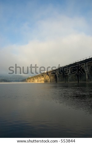 Stone arch railroad bridge crossing a river with fog and mist.