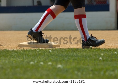 A softball player standing on base ready to run.
