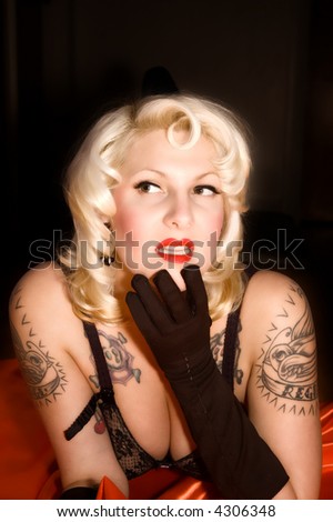A blond woman with a black vintage bra, black gloves, and tattoos looking to the side.