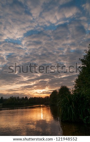 View on evening glow of cloudy sky over river with sunset reflection in water
