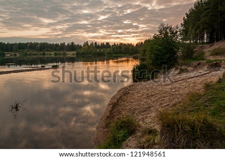 Evening glow of cloudy sky over river valley with sunset reflection in water
